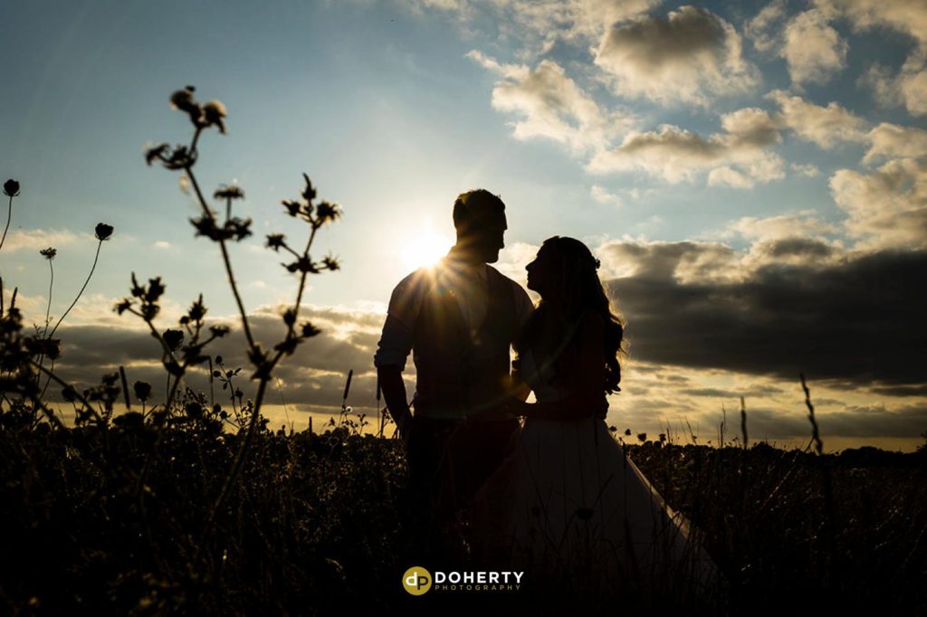 Silhouette photo of bride and groom in a field at sunset