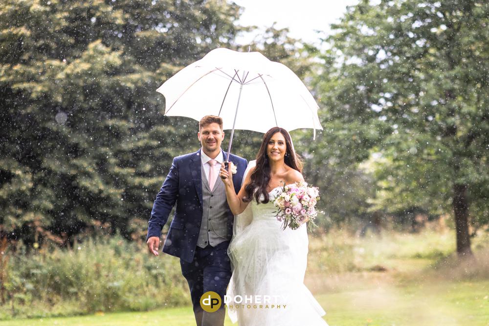Bride and groom walking in rain under umbrella