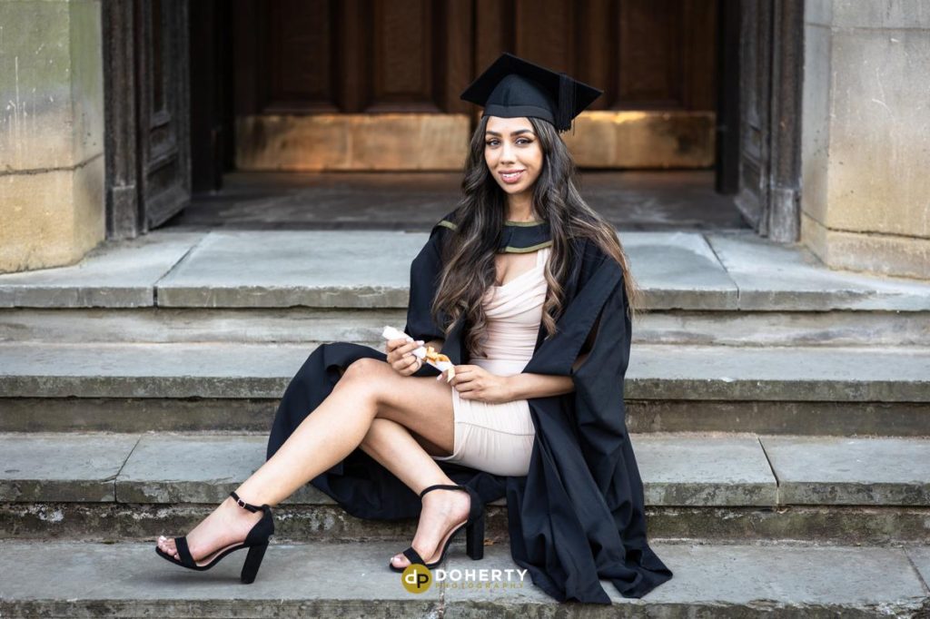 Graduation photo of young woman sitting down on steps at Birmingham University