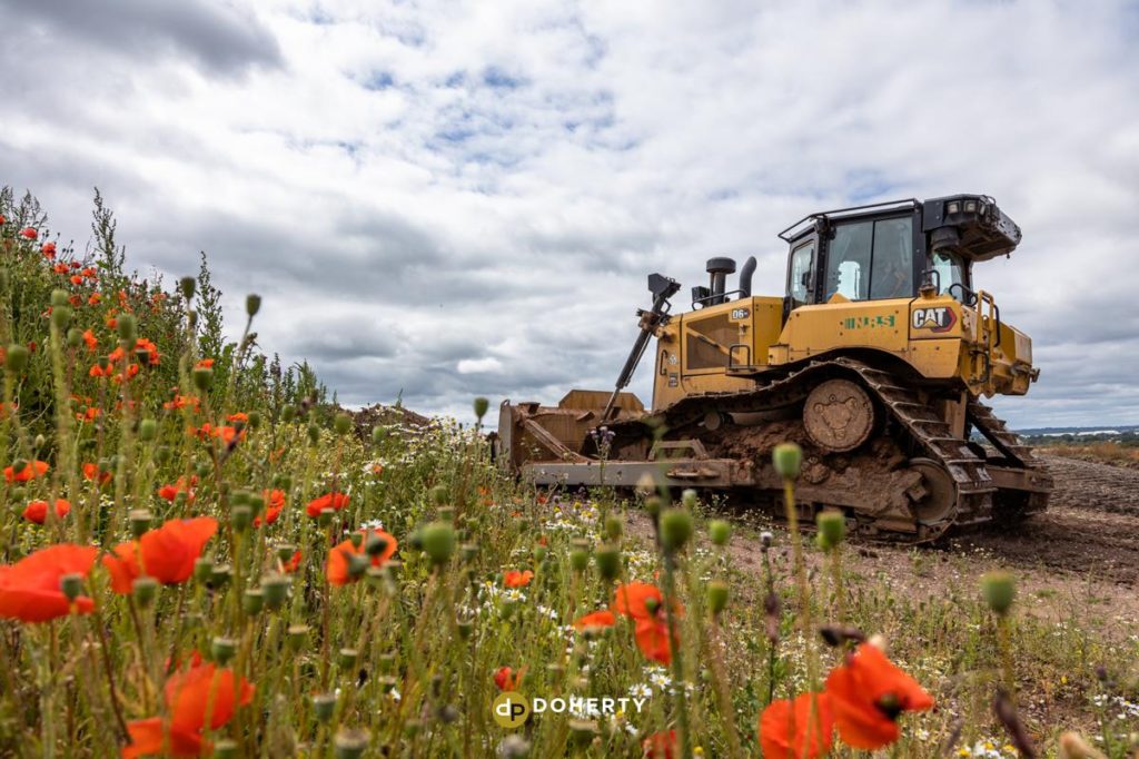 Digger drives past flowers in foreground on a quarry