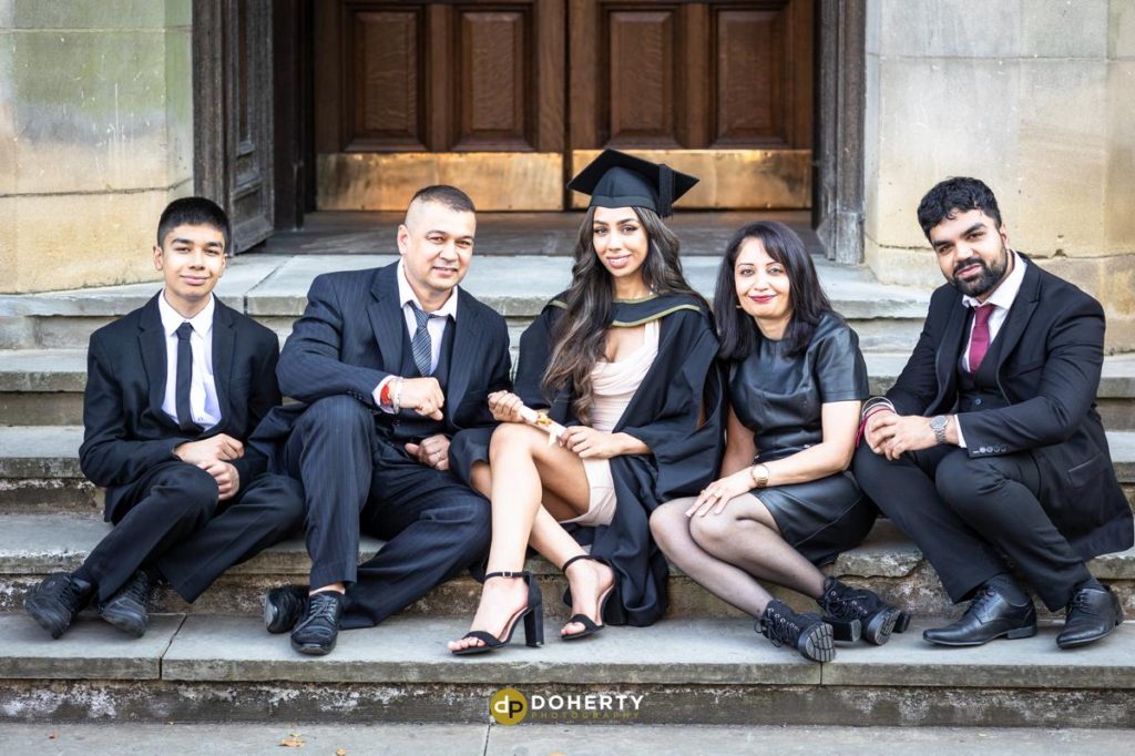 Graduation photo of young woman with family sitting on steps at Birmingham University
