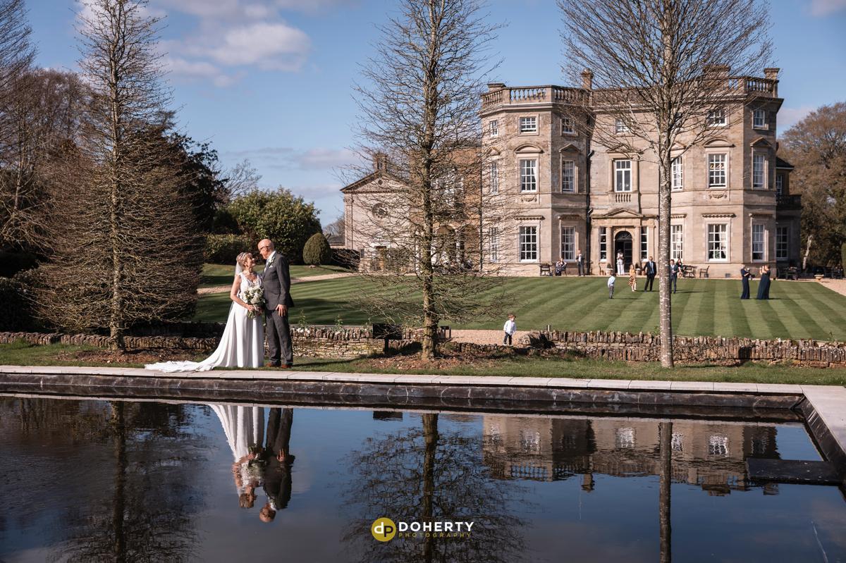 Bourton Hall with bride and groom at the pond with house as a backdrop